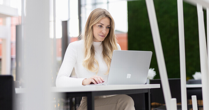 Frau sitzt an einem Tisch und arbeitet am Laptop.