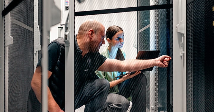 Zwei Menschen diskutieren sitzend vor einem Server in einem Serverraum.
