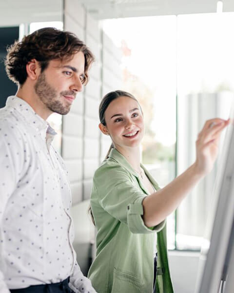 Zwei junge Menschen arbeiten mit dem Flipchart in einer freundlichen, hellen Büroumgebung.