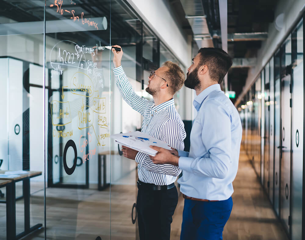 Two men writing on a glass wall