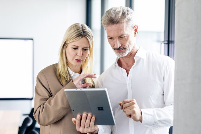 Zwei Personen besprechen gemeinsam Informationen auf einem Tablet in einer modernen Büroumgebung.