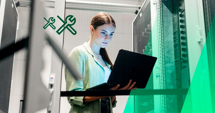 Eine junge Frau hält in den Händen offenen Laptop und arbeitet damit in einem Serverraum.