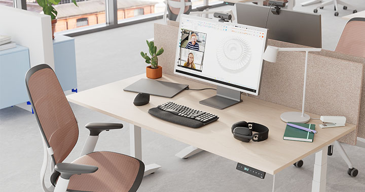 Modern workspace with height-adjustable desk and video conference displayed on the monitor