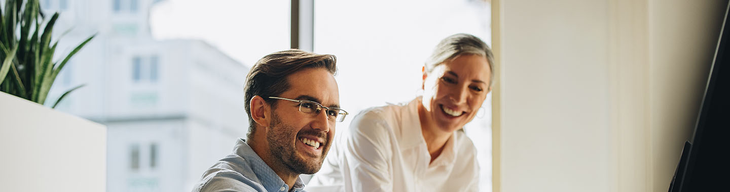 Man sitting on desk working. Woman talk to him.
