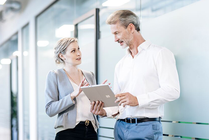 Two persons discussing information together on a tablet in a modern office environment.