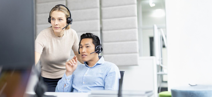Zwei Kolleg:innen arbeiten am Bildschirm, beide tragen Headsets